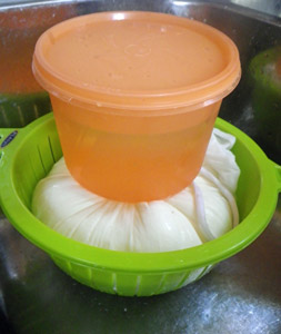 A container of water placed on the bag speeds drainage of the whey.